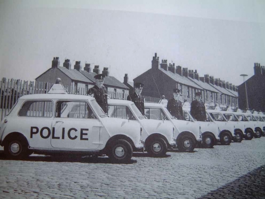 Historic side view of a long line of Liverpool Police Minis with officers